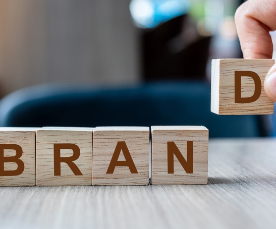 Businessman hand holding wooden cube block with BRAND business word on table background. Marketing, Advertising and Product development concept
