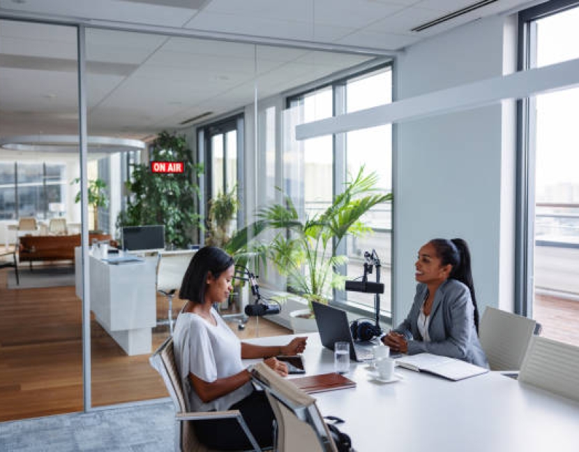 Waist-up portrait of a professional multi-ethnic female business manager with a friendly smile engaging in a podcast recording in a corporate environment.
